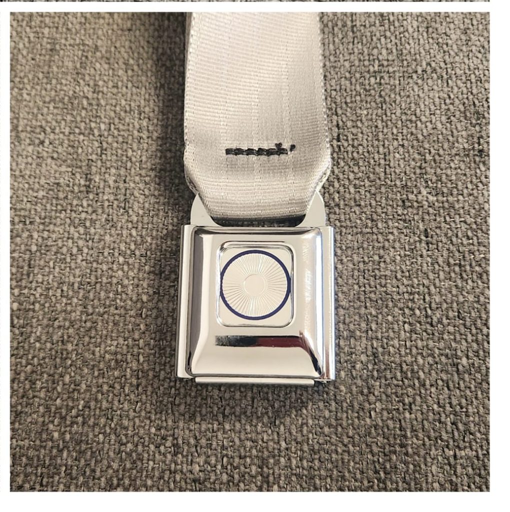 A chrome seatbelt buckle on a grey fabric